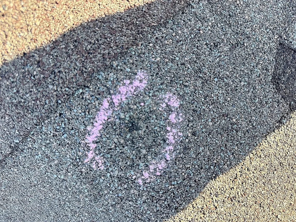 Pink chalk marking a hail impact on a shingle