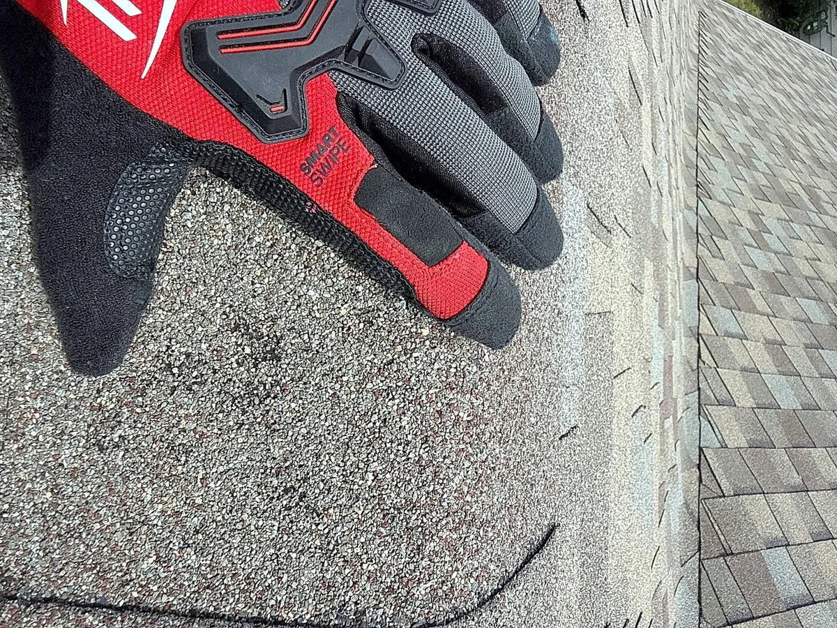 Gloved hand indicating damage on a shingle
